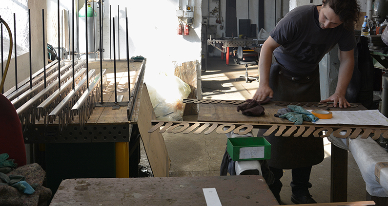 In der Werkstatt von Rüdiger Lüst patiniert Mitarbeiter Keoma Slavik die Ziffern, damit das Messing älter wirkt.