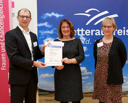Tina Trede (v.l.) und Anette Schönberger nehmen die Auszeichnung „Familienfreundliches Unternehmen Wetterau“ aus den Händen von Landrat Jan Weckler entgegen.