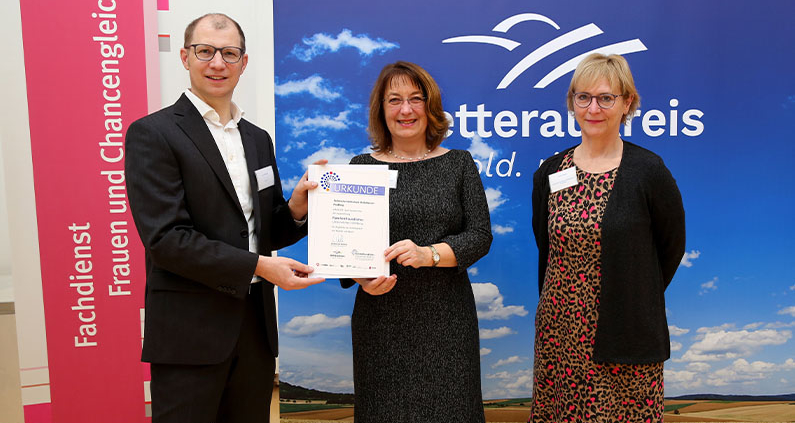 Tina Trede (v.l.) und Anette Schönberger nehmen die Auszeichnung „Familienfreundliches Unternehmen Wetterau“ aus den Händen von Landrat Jan Weckler entgegen.